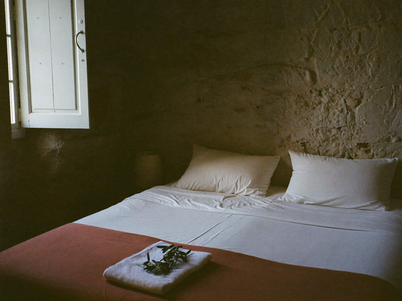 Freshly made guest room in a Gozo guesthouse, bed with folded towel and olive sprig in morning light